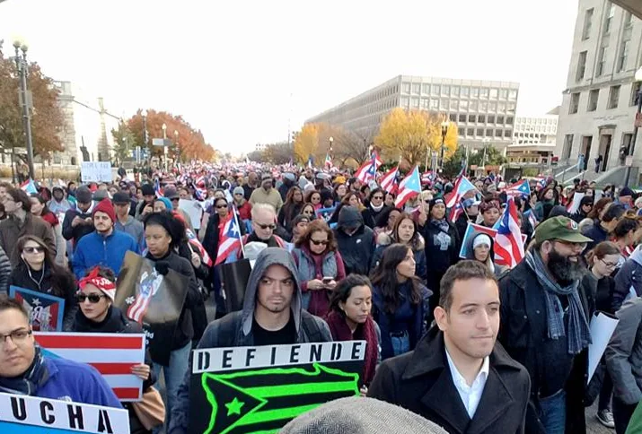 Gabriel Franco marching in a large crowd carrying Puerto Rican flags